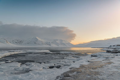 Scenic view of snowcapped mountains by sea against sky during sunset