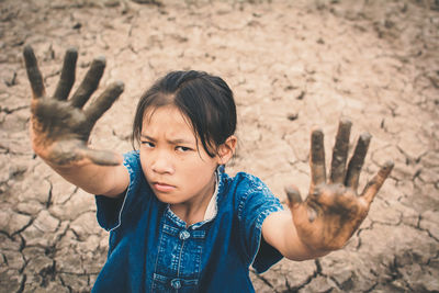High angle portrait of girl showing dirty hands on cracked field