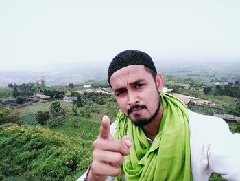 Portrait of young man wearing topi against sky over landscape