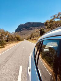 Road by mountain against clear blue sky from car