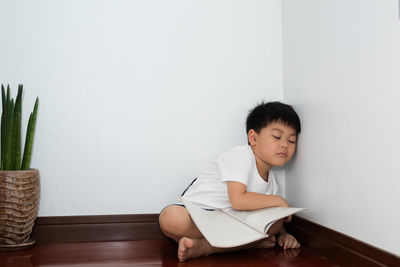 Boy looking away while sitting on wall at home