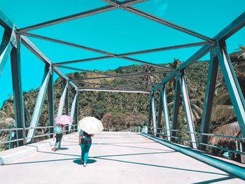 Rear view of men walking on bridge against blue sky