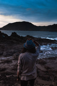 Rear view of man standing at beach against cloudy sky