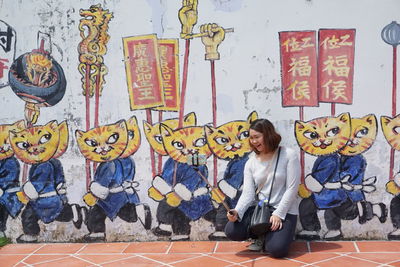 Smiling young woman taking selfie with mobile phone against wall