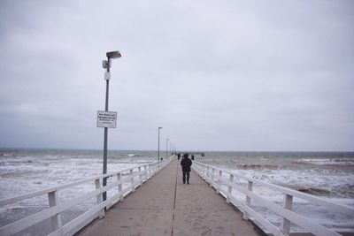 Rear view of man walking on beach against sky