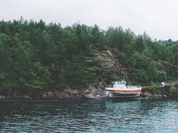 Boat sailing on river by trees against sky