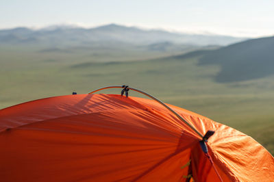 Tent on mountain against sky. part of the orange tent against background of a blurred hilly valley