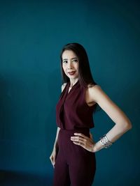 Portrait of a young woman standing against blue background