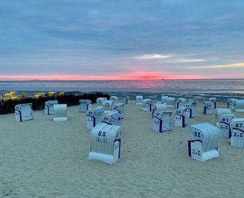 Hooded chairs on beach against sky during sunset
