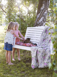 Girls stroking cat on hanging bench