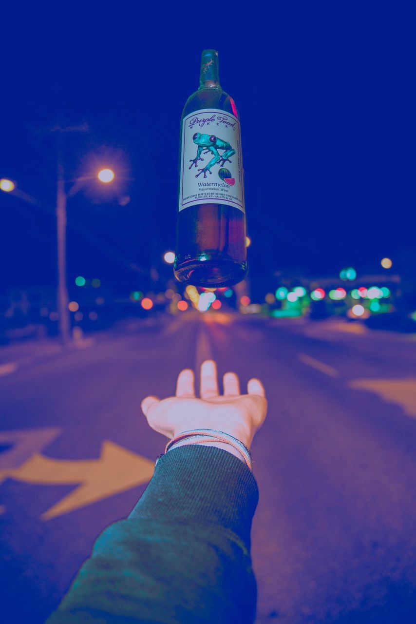 night, human hand, real people, illuminated, human body part, one person, street, outdoors, focus on foreground, transportation, land vehicle, lifestyles, close-up, road, men, sky, clear sky, city, tree, people