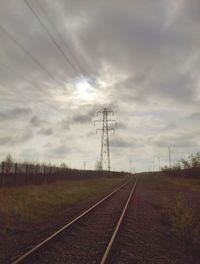 Railroad tracks on field against cloudy sky