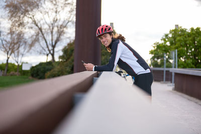 Portrait of smiling man using phone while standing on bridge