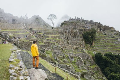 A man in a yellow jacket is standing near ruins of machu picchu, peru