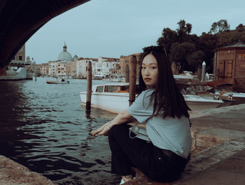 Portrait of woman sitting by canal against sky