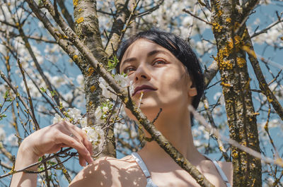Beautiful brunette girl sitting on a flowering cherry tree. spring, beauty, woman health concept.