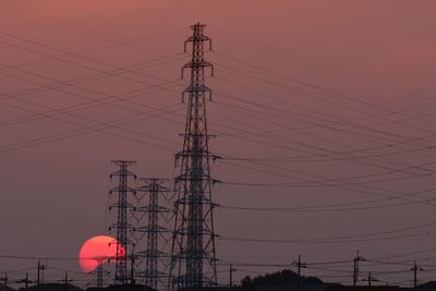 Low angle view of electricity pylons against sunset