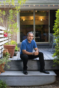 Smiling hispanic man sit on deck in front of his house