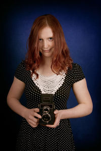 Portrait of young woman holding camera against blue background