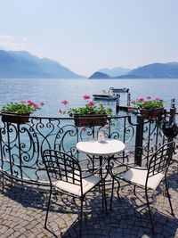 Empty chairs and table by sea against sky