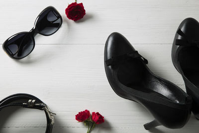 High angle view of pump shoes by roses and belt with sunglasses on hardwood floor