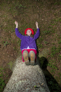 Woman with arms raised sitting on tree trunk