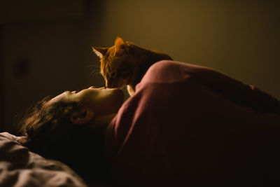 Woman kissing cat while lying on bed at home