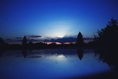 Silhouette trees by lake against blue sky during sunset