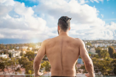 Rear view of shirtless man in city against sky