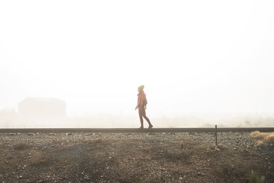 Side view of woman walking on field against clear sky