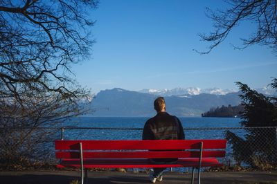 Rear view of man sitting on bench on promenade against blue sky