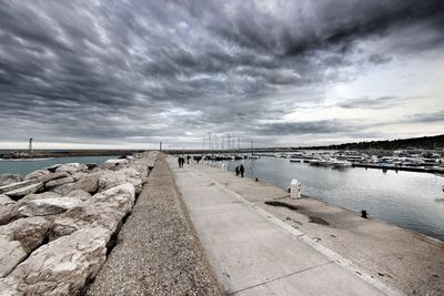 People walking on jetty against clouds