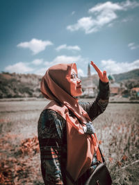 Rear view of woman with arms raised standing on field against sky