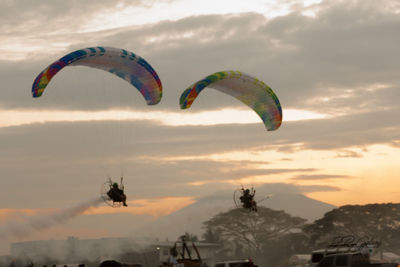 Low angle view of people paragliding against sky during sunset