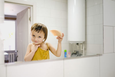 Child in yellow jumpsuit combs his own in front of mirror in bathroom