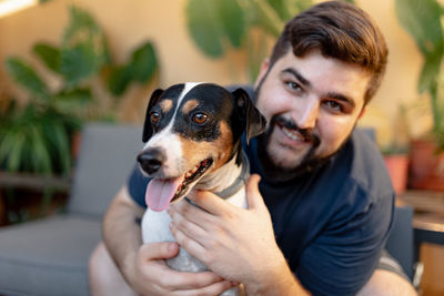 Friendly young man hugging his cute grocer dog and looking at camera. the dog has the tongue out