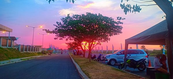 Cars on street in city against sky at sunset