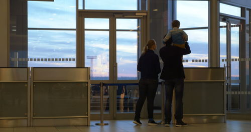 Rear view of people standing by window