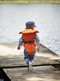 Boy wearing life vest walking on jetty