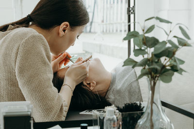 A girl cosmetologist extends eyelashes to a woman.