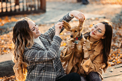 Two happy female friends girls having fun with cute cocker spaniel puppy in autumn park. two