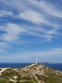 Lighthouse by sea against cloud strewn  sky