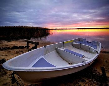 Boat moored on beach against sky during sunset