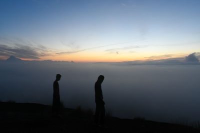 Silhouette men standing on land against sky during sunset