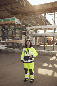 Portrait of female blue-collar worker with hardhat standing outside industry