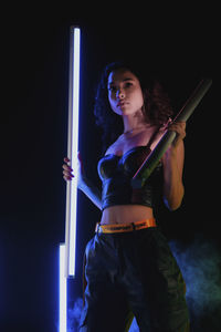 Young woman looking away while standing against black background