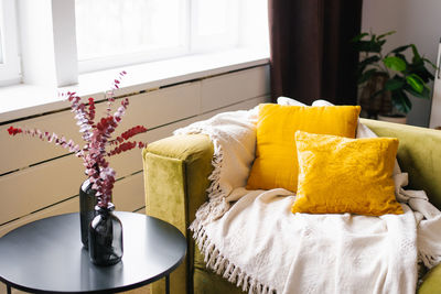 Yellow pillows on a green sofa with eucalyptus branches in vases on the table, interior living room.