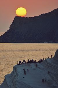 People on mountain by sea during sunset