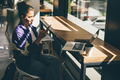 Full length of man using mobile phone while sitting on table