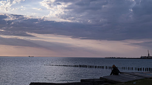 Rear view of man sitting by sea against sky during sunset